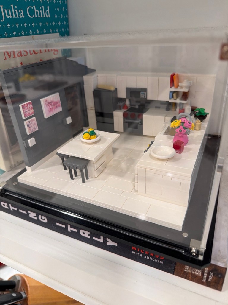 Custom LEGO replica of Wendi and Dan’s kitchen featuring the large white island, refrigerator, stove, stools, flowers and small lemons.