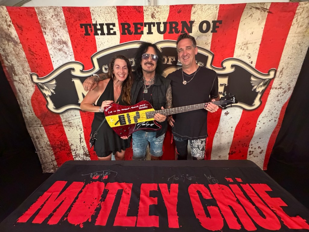 Wendi and Dan posing with Nikki Sixx and their newly signed bass guitar at a Mötley Crüe meet-and-greet.