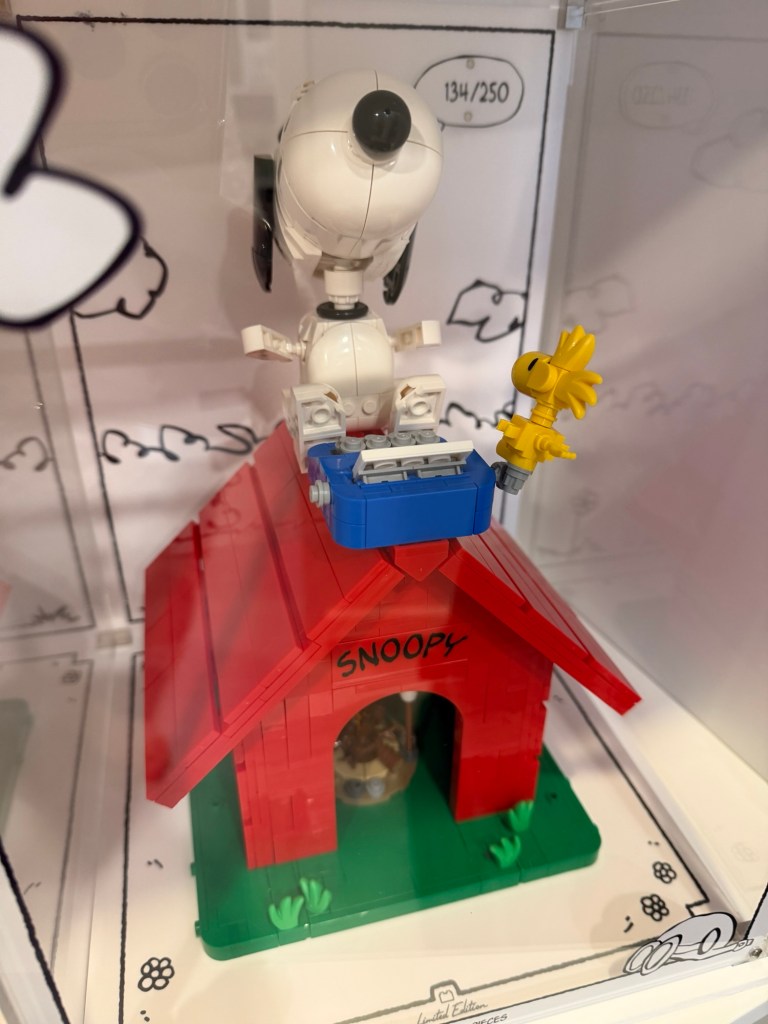 LEGO Snoopy sitting on top of his red doghouse with a blue typewriter and Woodstock beside him.