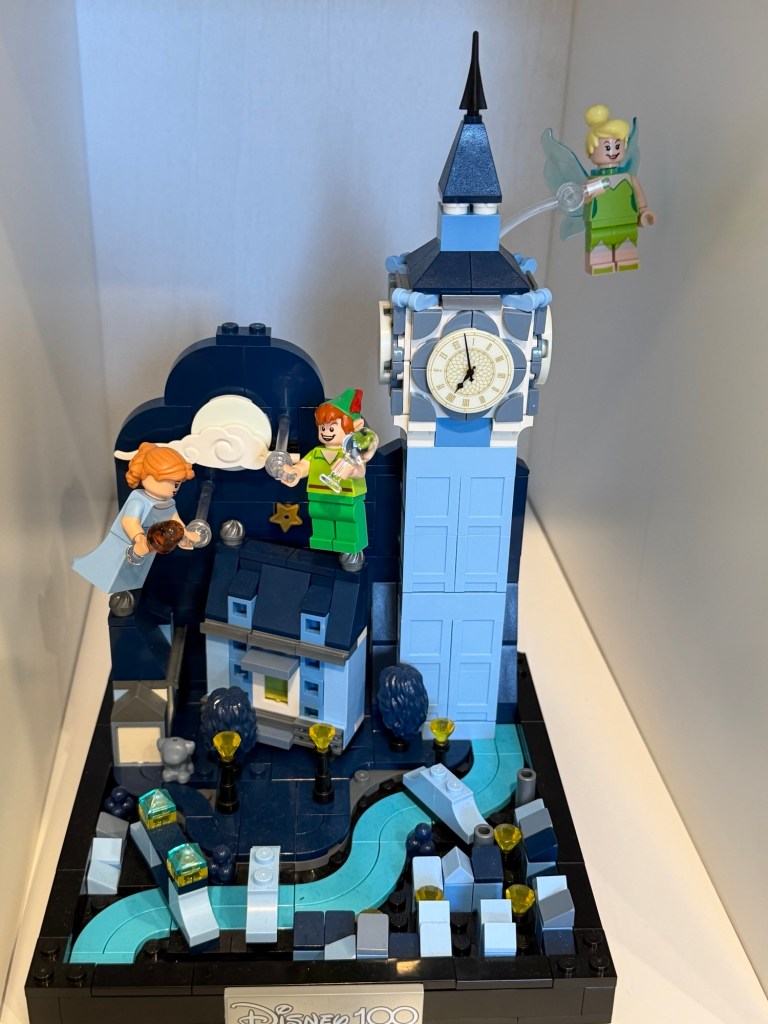 LEGO Peter Pan scene with Wendy, Peter Pan and Tinker Bell beside a blue clock tower under a nighttime sky.