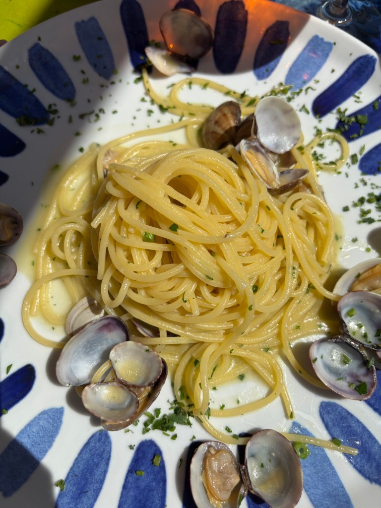 Spaghetti with clams in their shells and chopped herbs, served on a blue-and-white patterned plate.