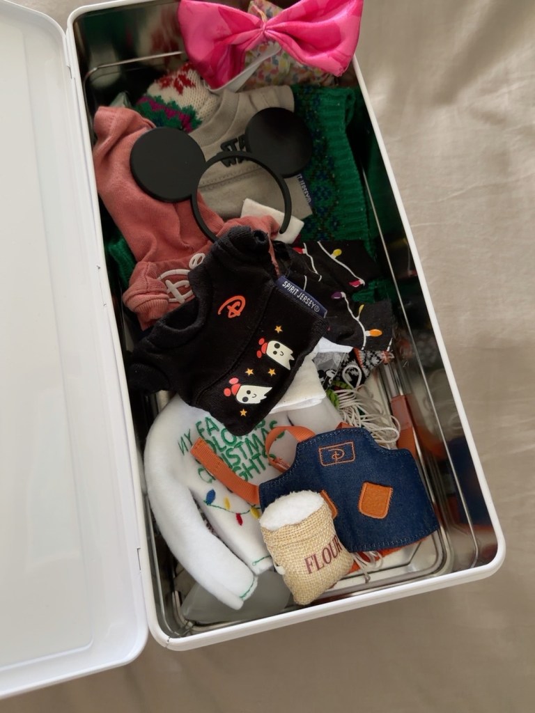 Snoopy's outfits and accessories stored inside a repurposed Veuve Clicquot case