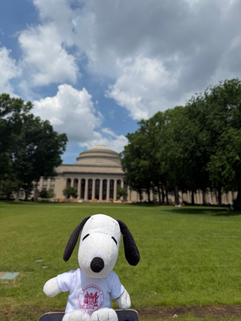 Snoopy wearing an MIT shirt in front of the Massachusetts Institute of Technology campus
