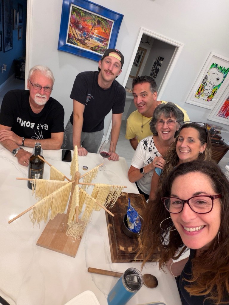 Family gathered around the kitchen island while homemade pasta dries on wooden racks.