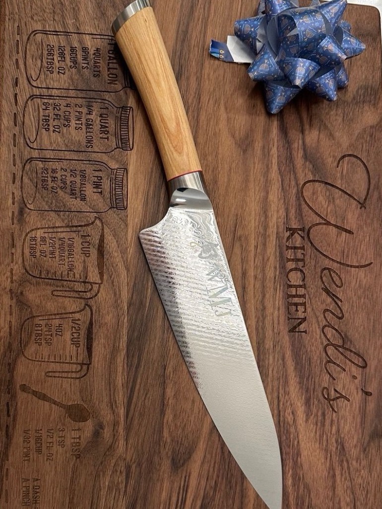 Personalized Wendi’s Kitchen wooden cutting board with a chef’s knife resting on top.